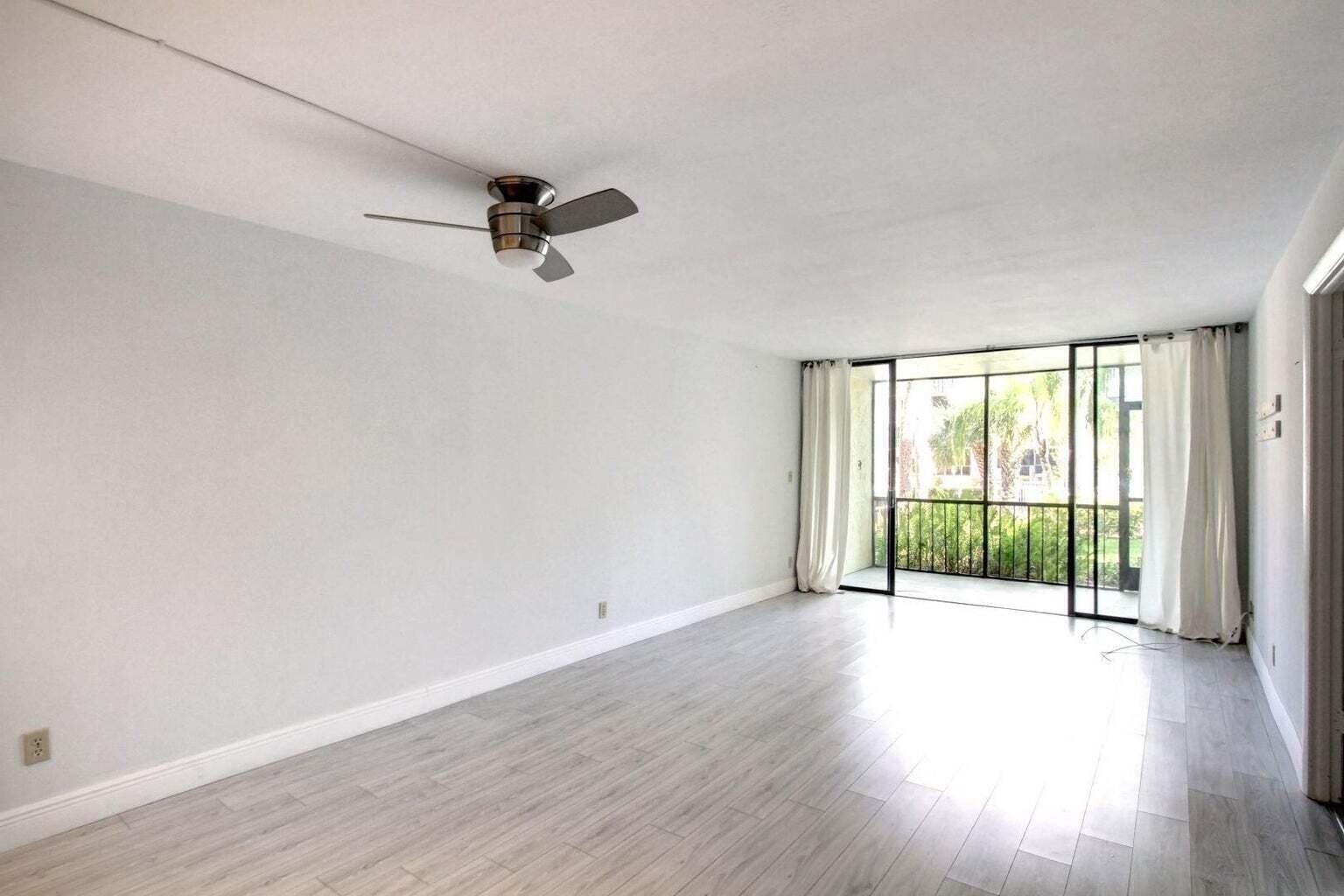 An empty living room with light wood-look flooring, a ceiling fan, and a screened balcony — 11 Royal Palm Way # 1040, Boca Raton FL 33432, BOCA RATON, FL