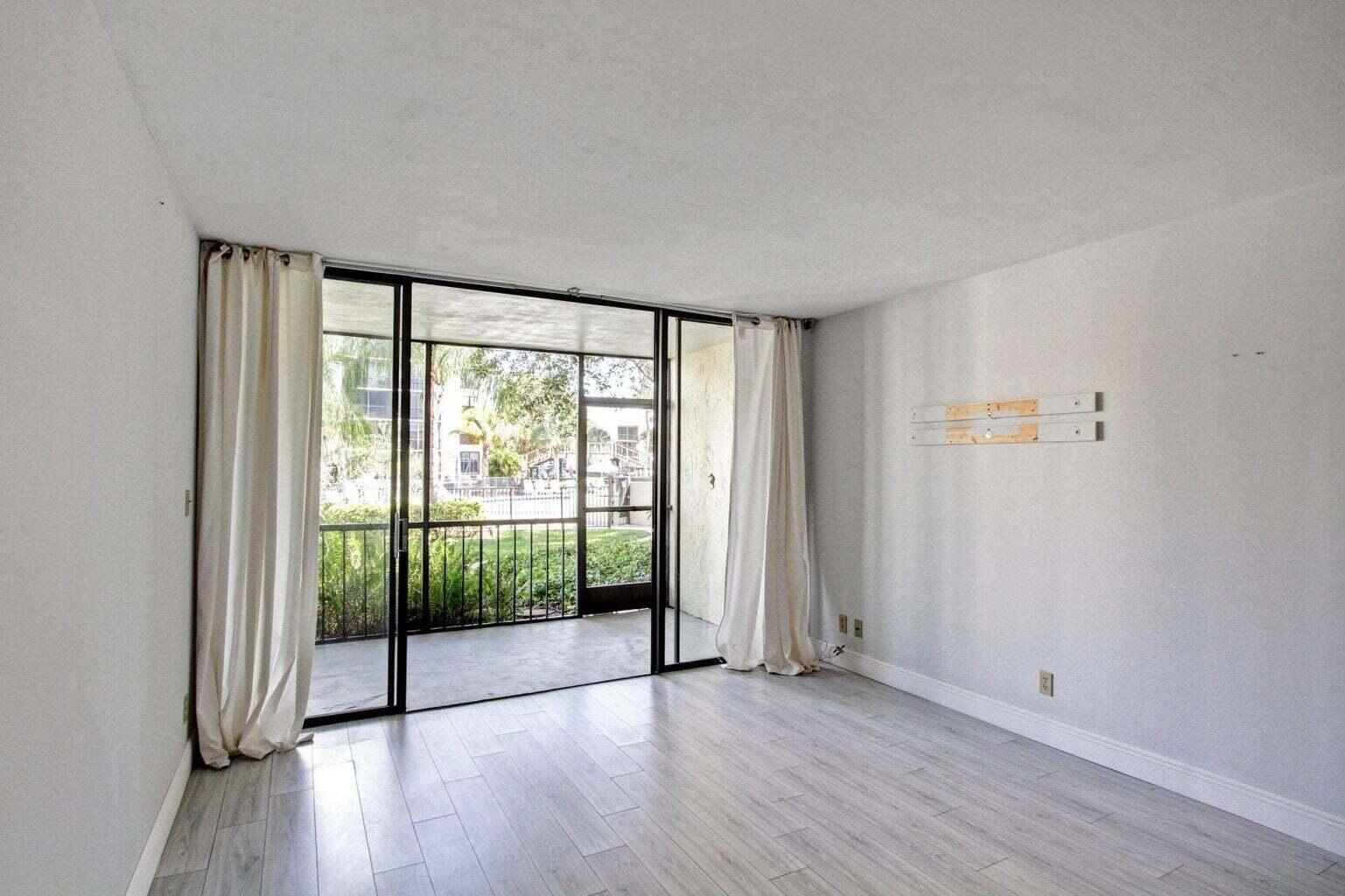 An empty living room with light wood-look flooring, white walls, and a sliding glass door — 11 Royal Palm Way # 1040, Boca Raton FL 33432, BOCA RATON, FL