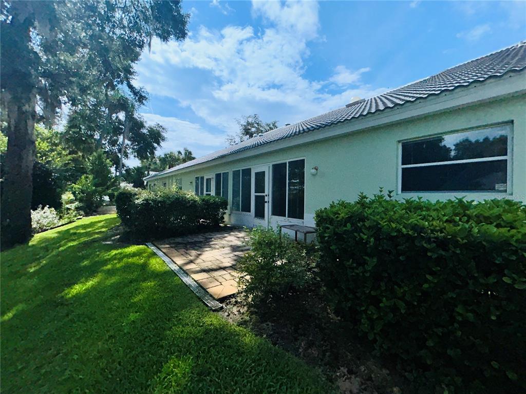 A paved patio sits beside a light-colored house with a tiled roof and green bushes — 806 WINDERMERE BOULEVARD, INVERNESS, FL