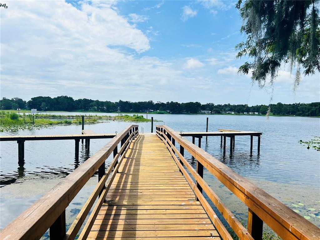 A wooden dock extends over a lake toward a distant tree-lined shore under a cloudy sky — 806 WINDERMERE BOULEVARD, INVERNESS, FL
