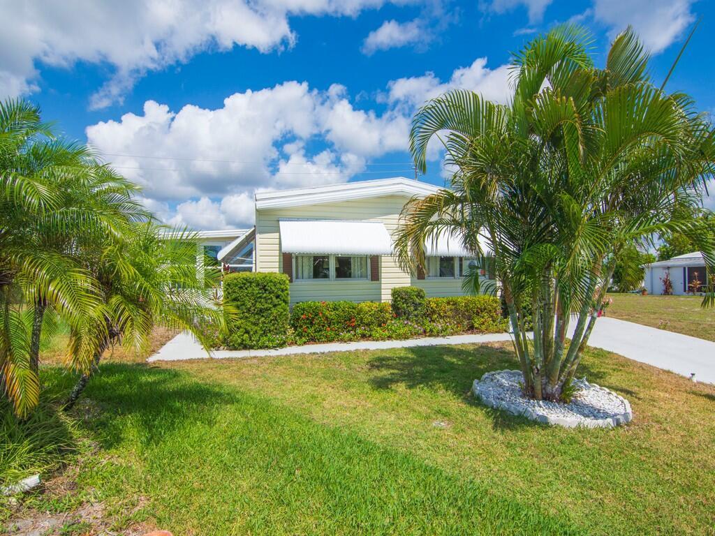 A light-colored manufactured home features white window awnings, a palm tree, and landscaped bushes — 196 NE Emerald Drive, Jensen Beach FL 34957, JENSEN BEACH, FL