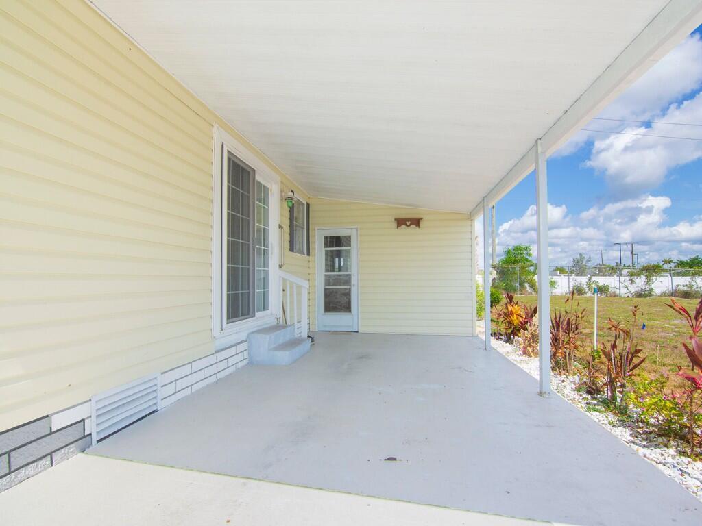 A covered concrete patio with light yellow siding, a sliding glass door, and a doorway — 196 NE Emerald Drive, Jensen Beach FL 34957, JENSEN BEACH, FL