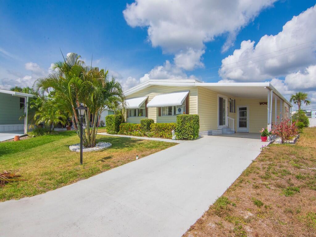 A light yellow mobile home with a concrete driveway, carport, and palm tree in front — 196 NE Emerald Drive, Jensen Beach FL 34957, JENSEN BEACH, FL