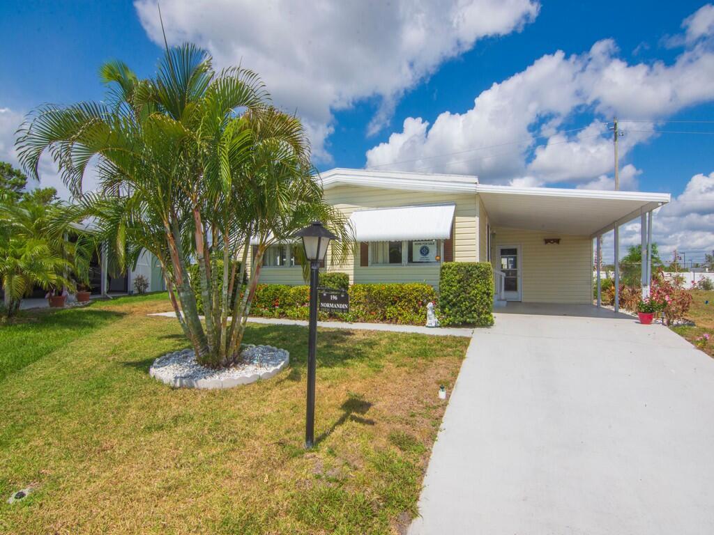 A light yellow manufactured home features a palm tree, a carport, and a concrete driveway — 196 NE Emerald Drive, Jensen Beach FL 34957, JENSEN BEACH, FL