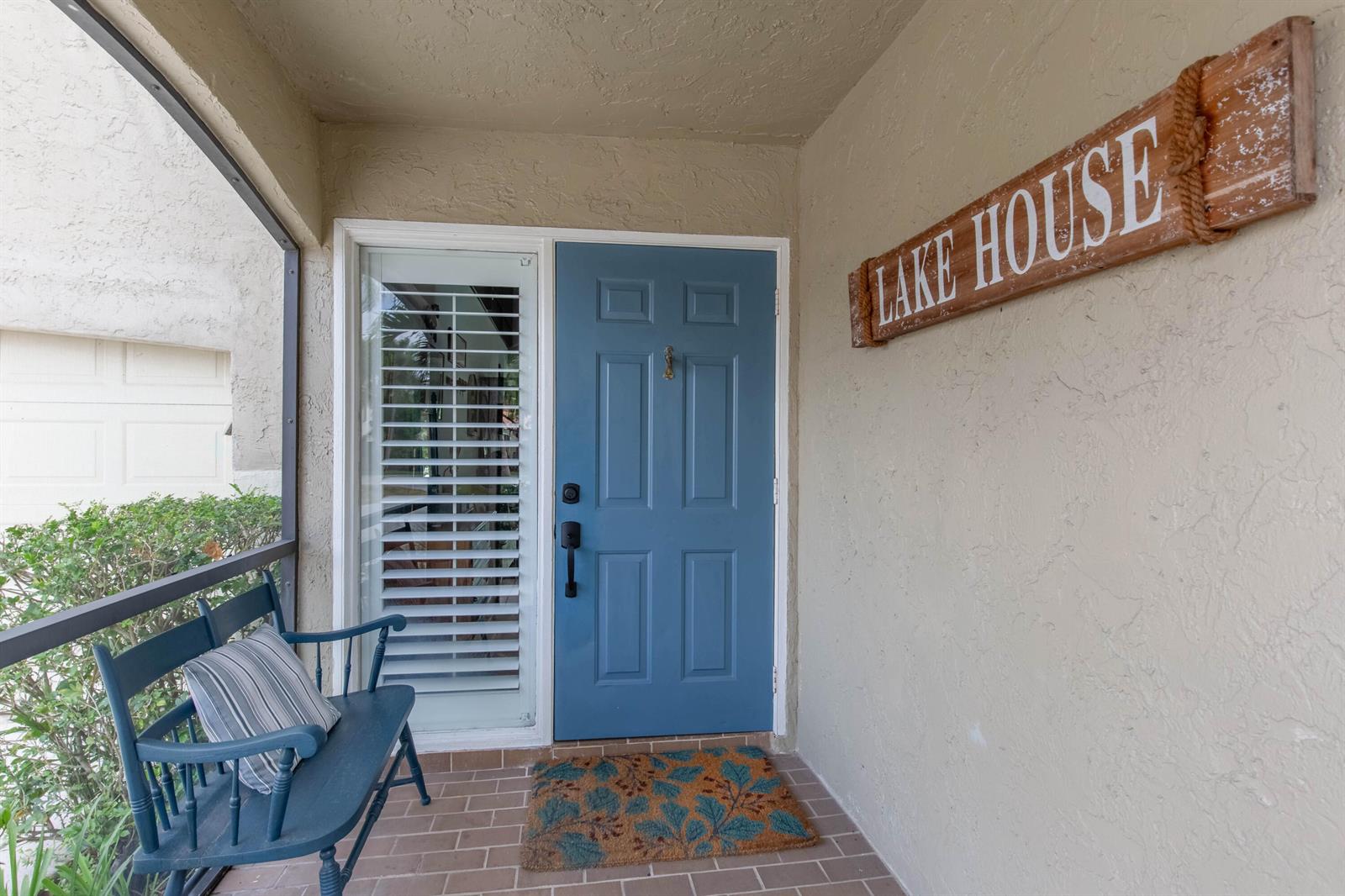 A blue front door and a bench sit on a covered porch with a sign — 1734 Harborside Circle, Wellington FL 33414, WELLINGTON, FL