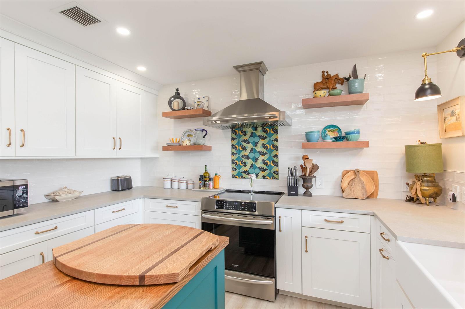 A white kitchen features a teal island, wood floating shelves, and a patterned tile backsplash — 1734 Harborside Circle, Wellington FL 33414, WELLINGTON, FL