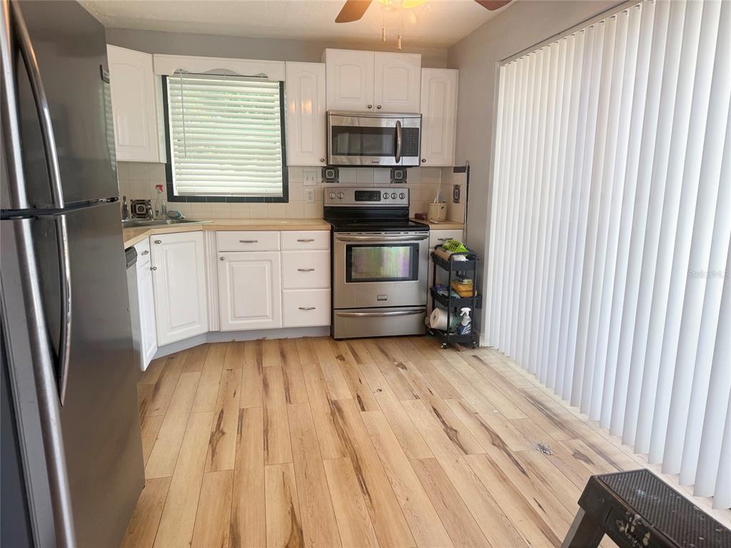 A kitchen features white cabinets, stainless steel appliances, and light wood-look flooring — 13157 CLAY AVENUE, LARGO, FL