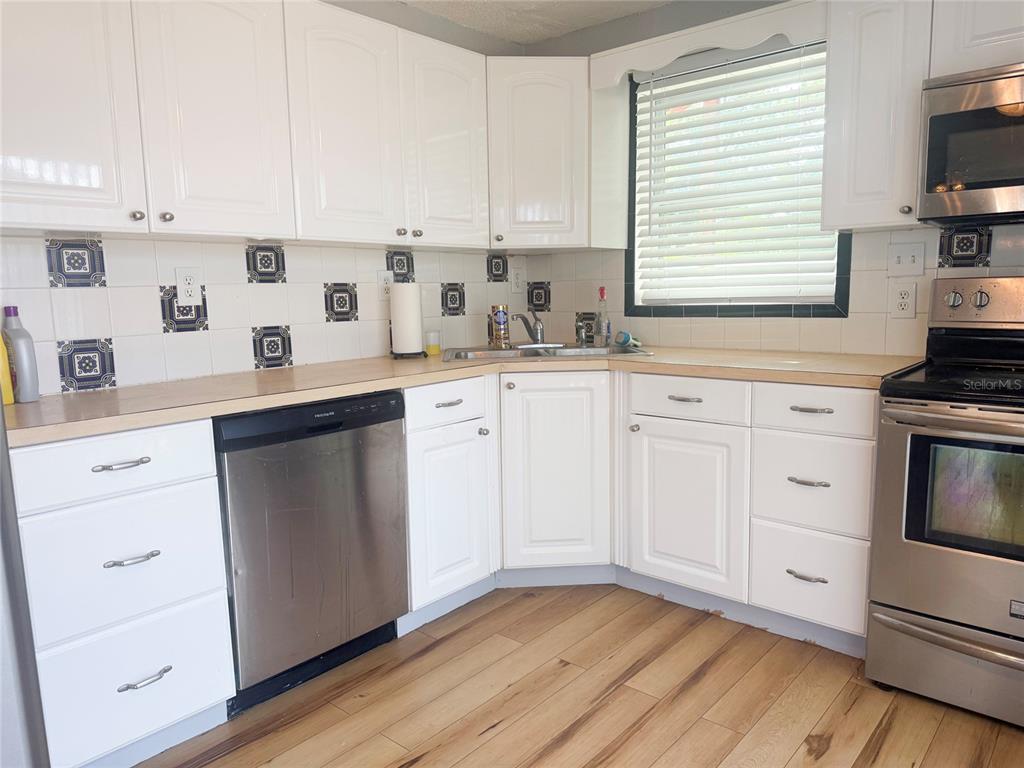 A kitchen features white cabinets, stainless steel appliances, wood-look flooring, and a tiled backsplash — 13157 CLAY AVENUE, LARGO, FL