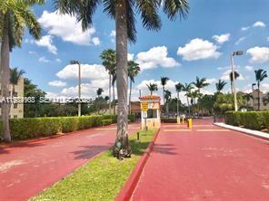 A gated entrance with a guardhouse, palm trees, and a red paved driveway — 6045 NW 186th St # 116, Hialeah FL 33015, HIALEAH, FL