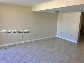 An empty room with beige walls, tile flooring, and a ceiling-mounted light fixture — 6045 NW 186th St # 116, Hialeah FL 33015, HIALEAH, FL