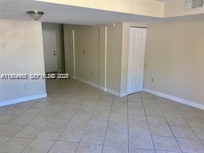 An interior view of a room with beige walls, tiled floors, and a white door — 6045 NW 186th St # 116, Hialeah FL 33015, HIALEAH, FL