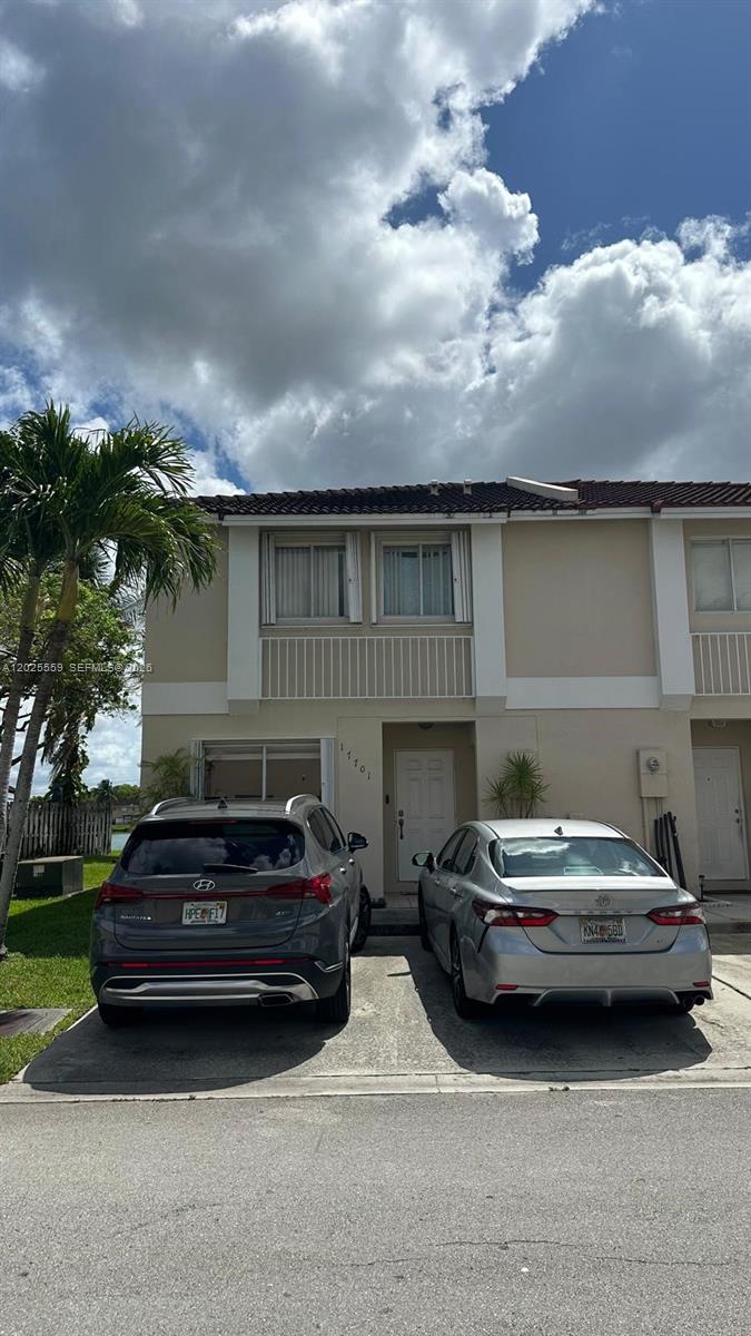 A two-story townhouse exterior features a beige facade with two cars parked in the driveway — MIAMI, FL