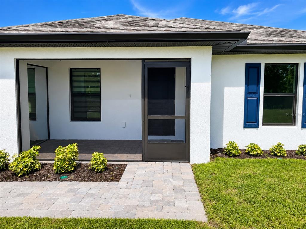 A white house exterior features a screened entryway, paver walkway, and blue window shutters — 93 PRESQUE ISLE DRIVE, PORT CHARLOTTE, FL