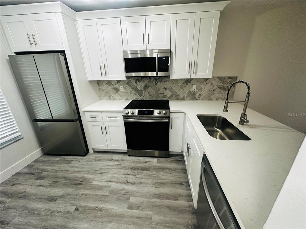 A modern kitchen features white cabinets, stainless steel appliances, and a gray herringbone tile backsplash — 3005 WAINWRIGHT COURT, NEW PORT RICHEY, FL