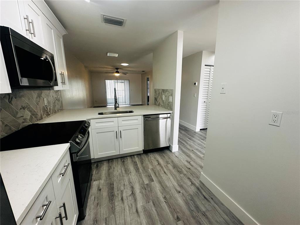 A kitchen features white cabinets, stainless steel appliances, a herringbone backsplash, and wood-look flooring — 3005 WAINWRIGHT COURT, NEW PORT RICHEY, FL
