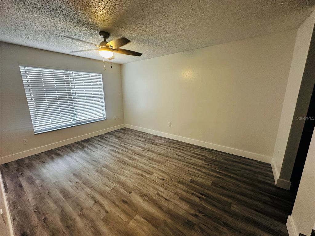 An empty room features wood-look flooring, a ceiling fan, and a window with blinds — 3005 WAINWRIGHT COURT, NEW PORT RICHEY, FL