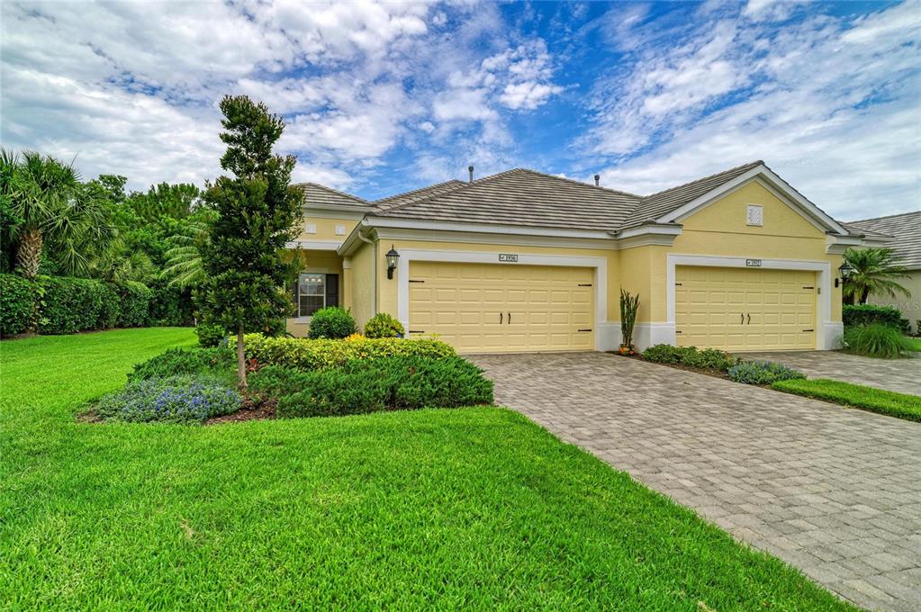 A yellow single-story house with two garage doors and a paved driveway sits on a lawn — 1936 ORANGE LAKE COVE, BRADENTON, FL