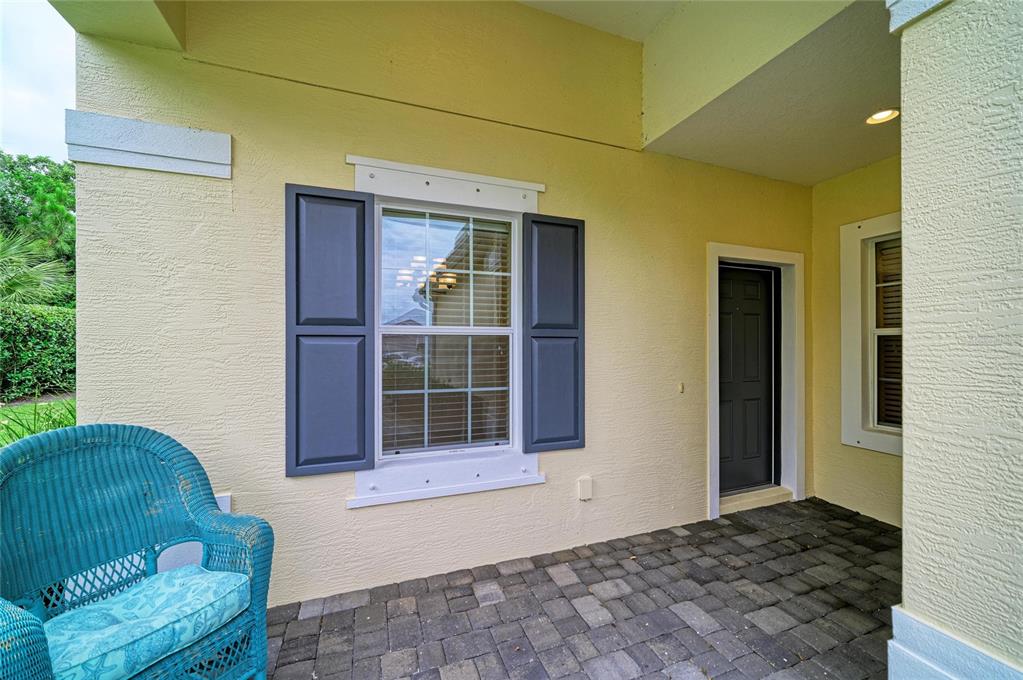 A covered patio features a blue wicker chair, a window with shutters, and a dark door — 1936 ORANGE LAKE COVE, BRADENTON, FL