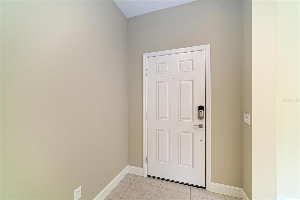 A white front door with a smart lock is centered in a tiled entryway — 1936 ORANGE LAKE COVE, BRADENTON, FL