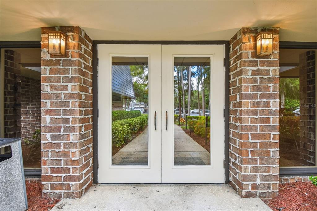 A double glass door entrance is framed by brick pillars with wall-mounted lanterns — 36750 US HIGHWAY 19 N UNIT 03116, PALM HARBOR, FL