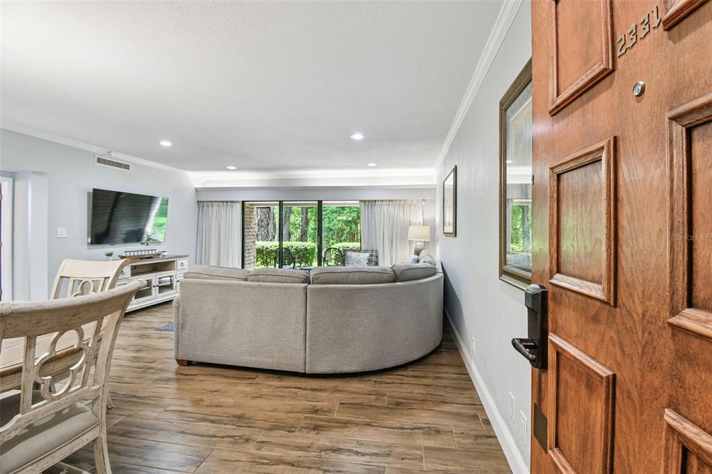 A view from an open front door into a living room with wood-look tile flooring — 36750 US HIGHWAY 19 N UNIT 03116, PALM HARBOR, FL