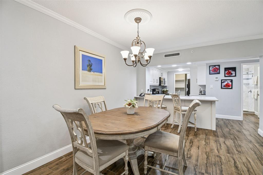 A dining area with a wooden table, chairs, and chandelier opens into a white kitchen — 36750 US HIGHWAY 19 N UNIT 03116, PALM HARBOR, FL