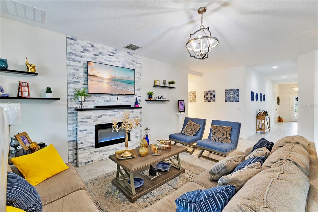 A living room features a stone fireplace, a wall-mounted television, and blue accent chairs — 3920 CABO ROJO DRIVE, ST CLOUD, FL