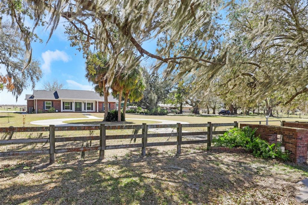 A brick house sits behind a wooden fence and large trees with Spanish moss — 3597 SE CO RD 760 ROAD UNIT 760, ARCADIA, FL