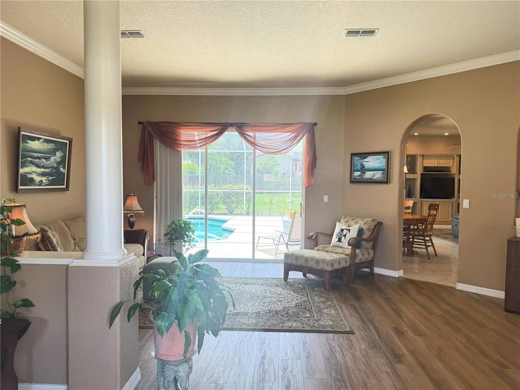 A living room with wood-look flooring, a white column, and sliding doors overlooking a pool — 7552 RIVER COUNTRY DRIVE, WEEKI WACHEE, FL