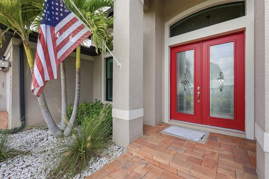 A red double front door with glass inserts sits beside a palm tree and flag — 9404 SPRING CIRCLE, PORT CHARLOTTE, FL