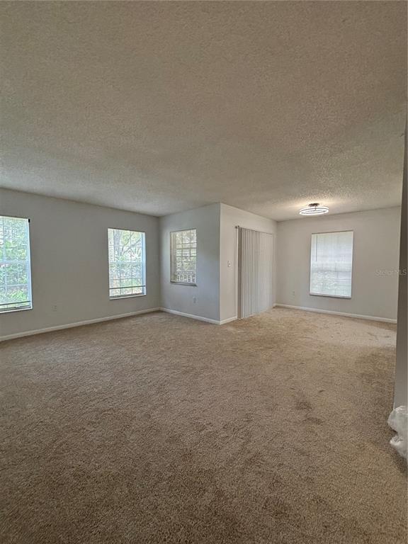An empty living room features beige carpeting, neutral walls, multiple windows, and a sliding glass door — 2690 CORAL LANDINGS BOULEVARD UNIT 615, PALM HARBOR, FL