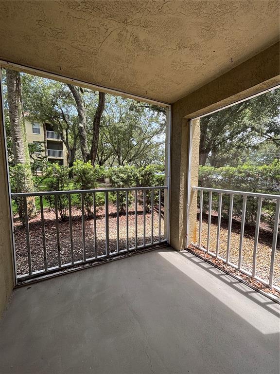 A screened-in balcony with a concrete floor and white metal railings overlooking trees and landscaping — 2690 CORAL LANDINGS BOULEVARD UNIT 615, PALM HARBOR, FL