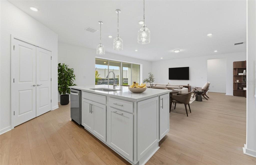 A kitchen island with a sink and pendant lights overlooks an open-concept living area — 9738 AUTUMN RIDGE AVENUE, RIVERVIEW, FL