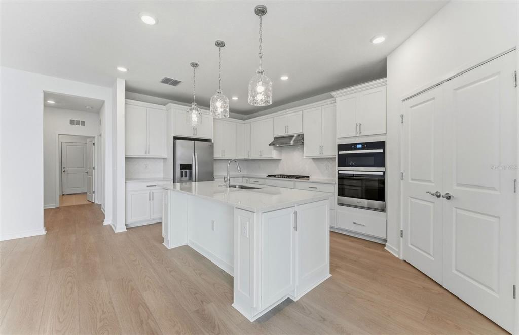 A bright kitchen features white cabinetry, a central island, stainless steel appliances, and light flooring — 9738 AUTUMN RIDGE AVENUE, RIVERVIEW, FL