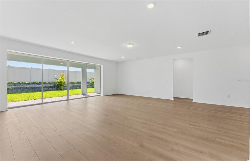 A spacious, empty room with light wood-look flooring, white walls, and large sliding glass doors — 9738 AUTUMN RIDGE AVENUE, RIVERVIEW, FL