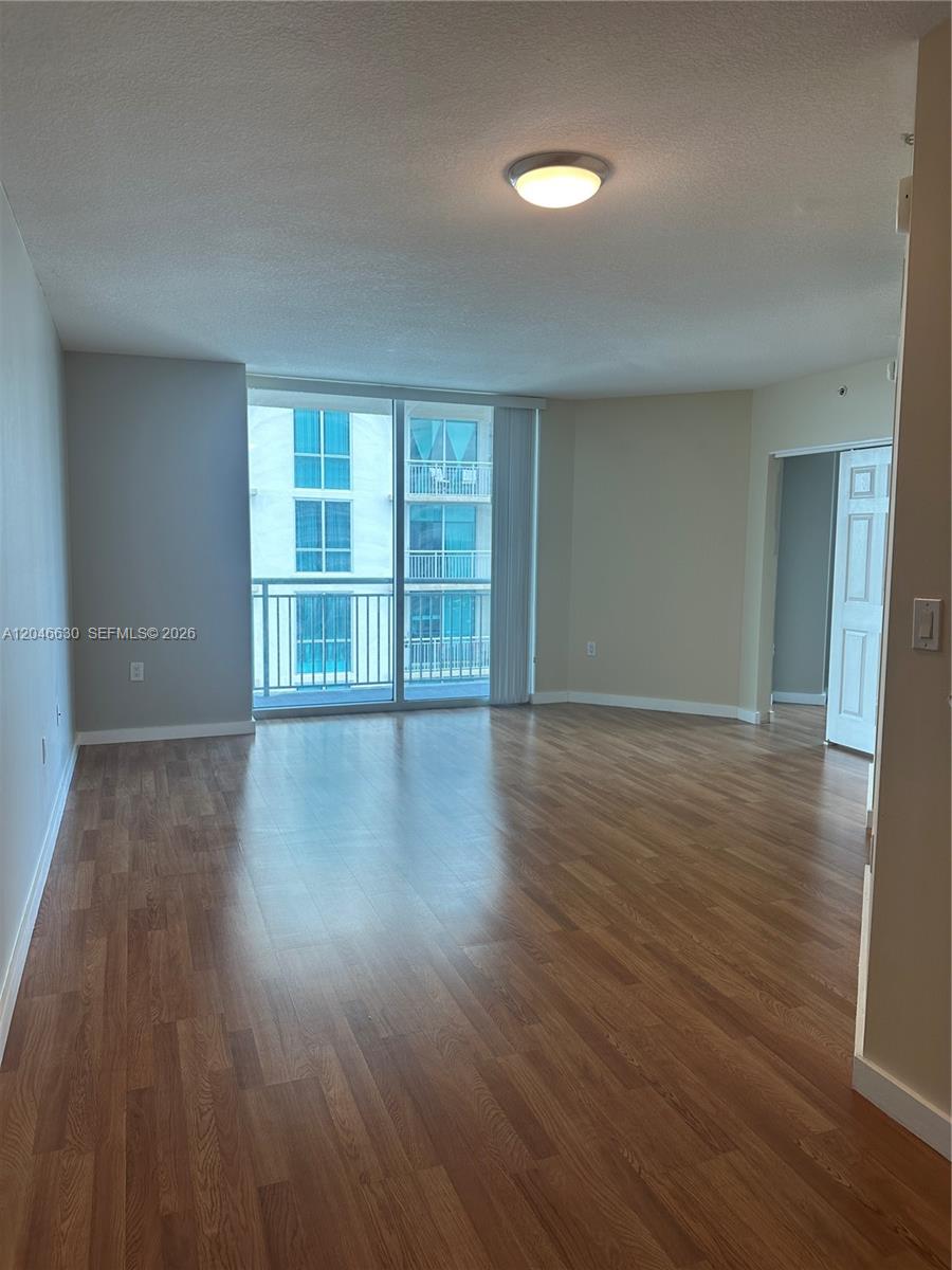 An empty living room features light wood-look flooring, a ceiling light, and a sliding glass door — 9066 SW 73rd Ct # 1903, Miami FL 33156, MIAMI, FL