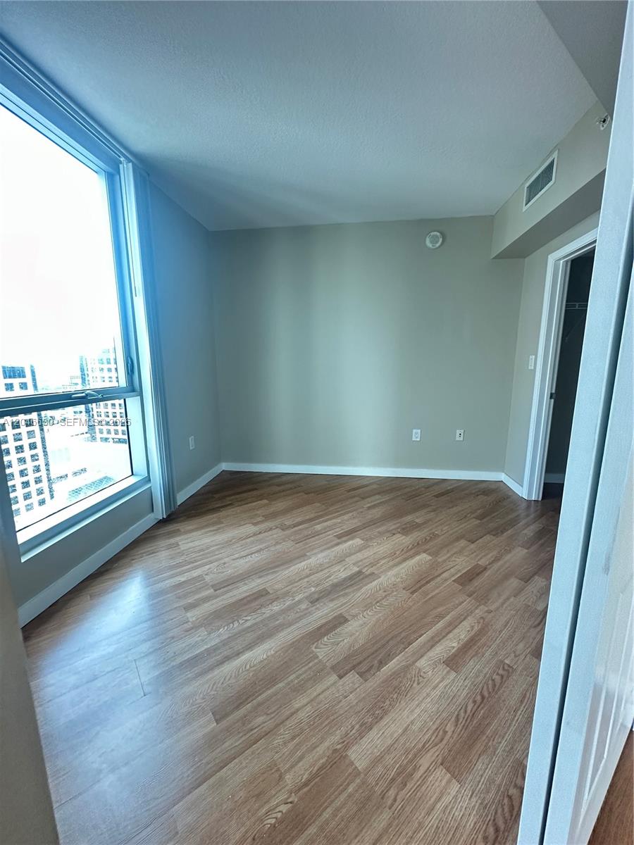 An empty bedroom features light wood-look flooring, beige walls, and a large floor-to-ceiling window — 9066 SW 73rd Ct # 1903, Miami FL 33156, MIAMI, FL
