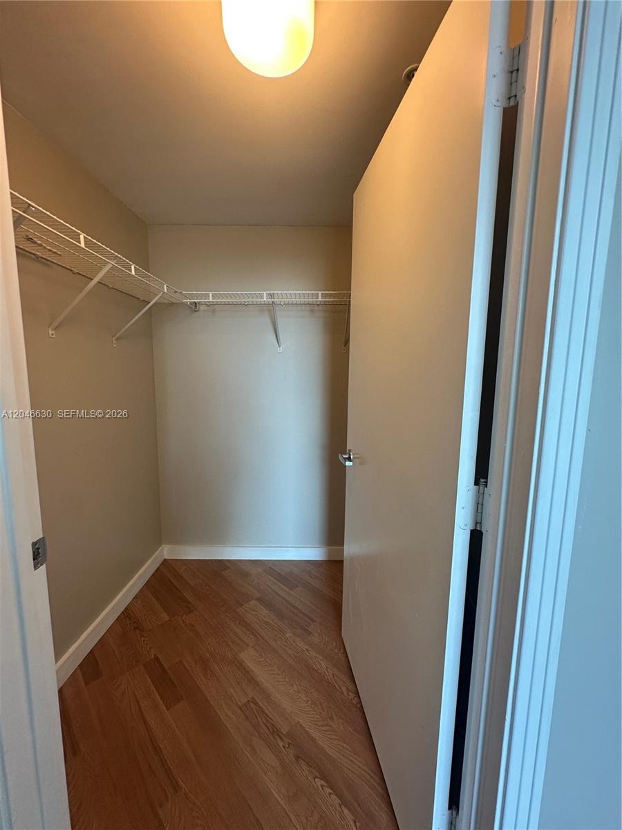 A walk-in closet features white wire shelving, beige walls, and wood-look laminate flooring — 9066 SW 73rd Ct # 1903, Miami FL 33156, MIAMI, FL