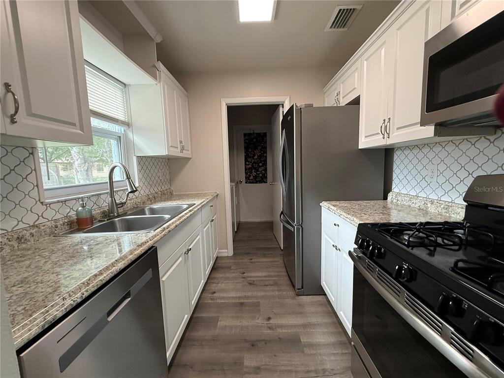 A galley kitchen features white cabinets, granite countertops, stainless steel appliances, and a tiled backsplash — 9129 SEWELL LANE, SPRING HILL, FL