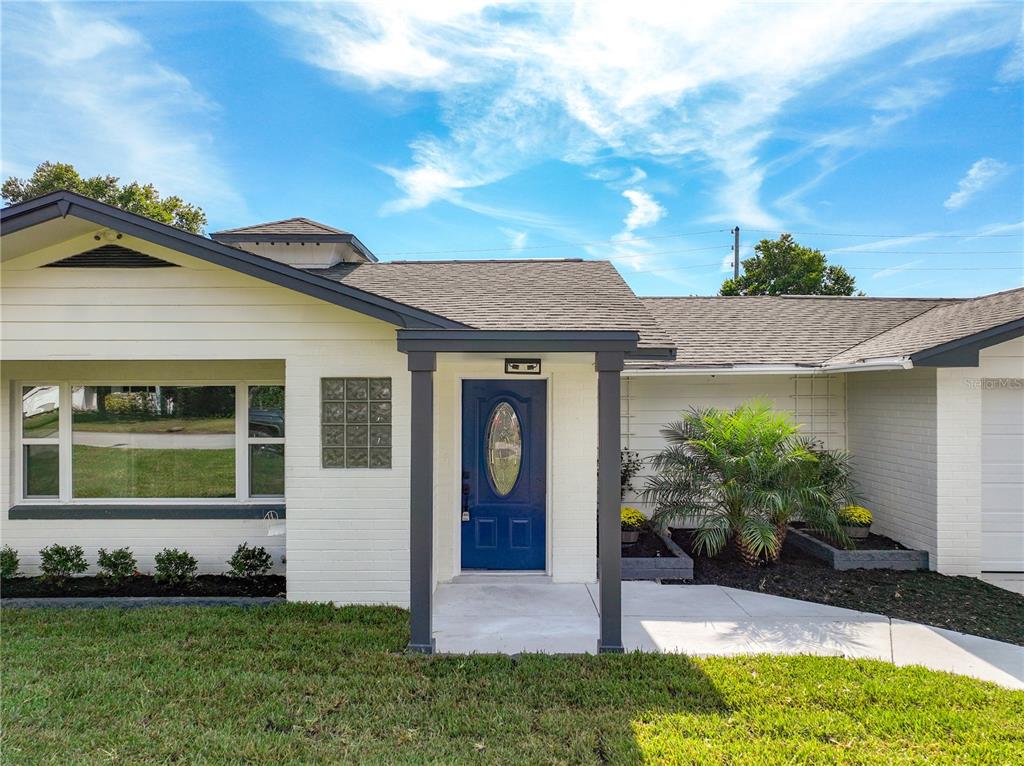 The exterior of a single-story house features white brick walls, a blue front door, and landscaping — 2680 PALMETTO ROAD, MOUNT DORA, FL