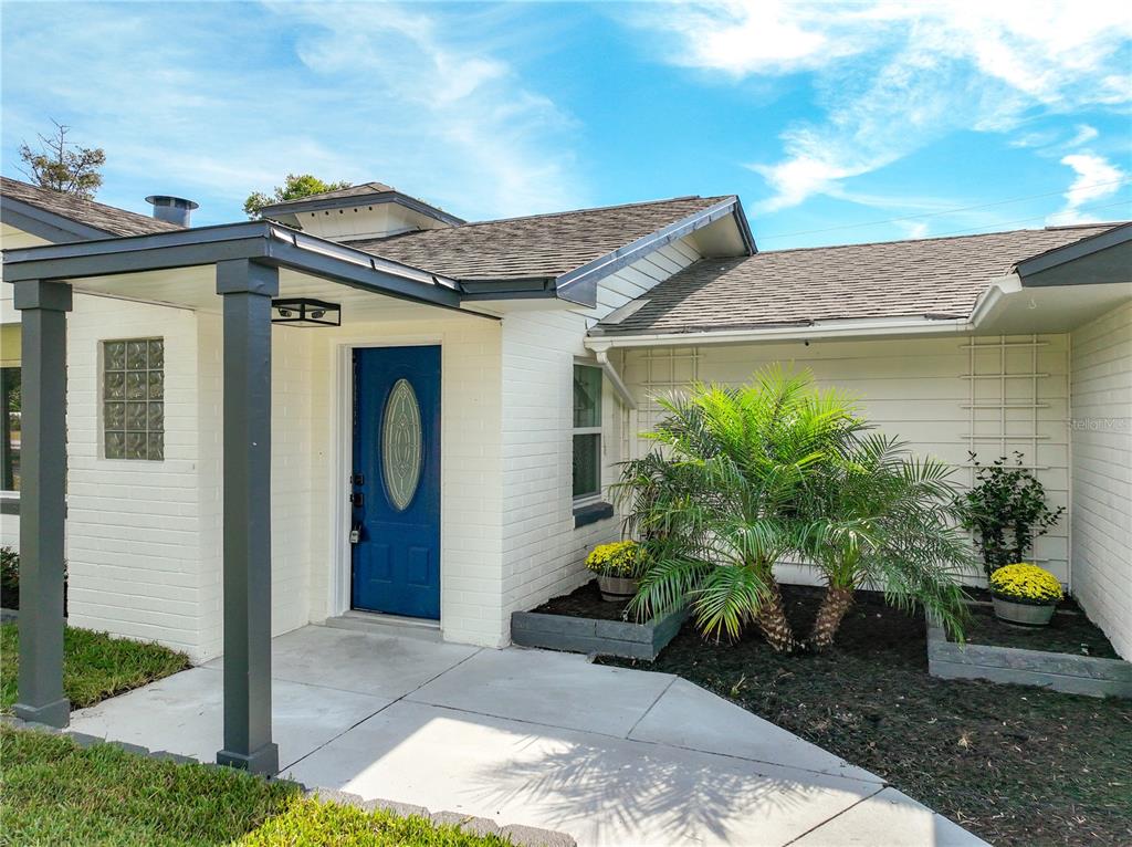 The exterior of a white brick house features a blue front door and a palm tree — 2680 PALMETTO ROAD, MOUNT DORA, FL