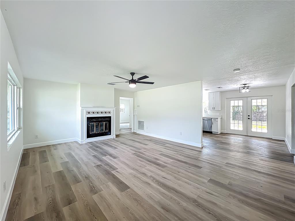 A living room with a fireplace, ceiling fan, and light wood-look flooring leads to a kitchen — 2680 PALMETTO ROAD, MOUNT DORA, FL