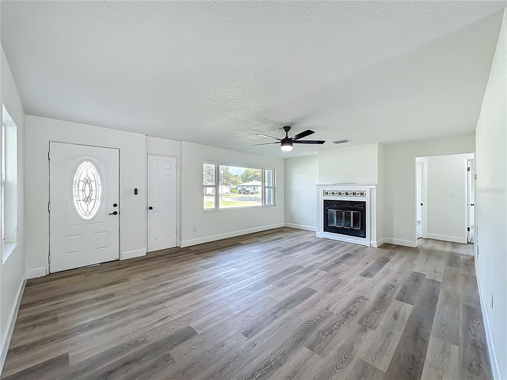 A living room with wood-look flooring, a white fireplace, a ceiling fan, and an entry door — 2680 PALMETTO ROAD, MOUNT DORA, FL