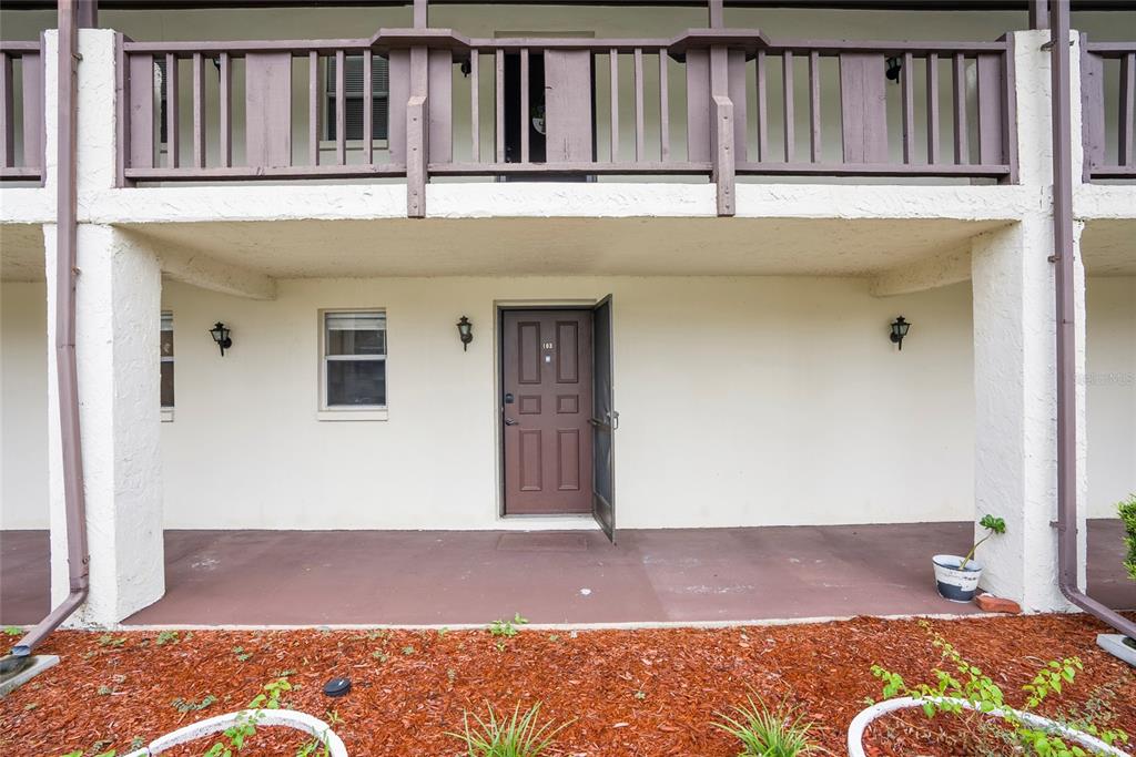 The exterior view shows a ground-level apartment entrance with a brown door and balcony above — 5521 BAY BOULEVARD UNIT 103, PORT RICHEY, FL