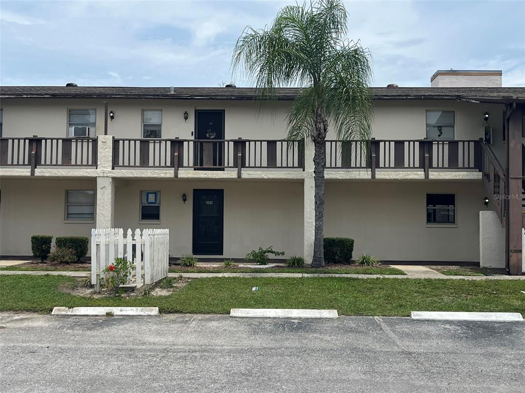 A two-story apartment building features a second-floor balcony, a palm tree, and a white fence — 5521 BAY BOULEVARD UNIT 103, PORT RICHEY, FL