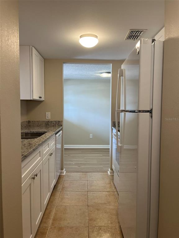 A galley kitchen with white cabinets, granite countertops, and a white refrigerator leads to another room — 5521 BAY BOULEVARD UNIT 103, PORT RICHEY, FL