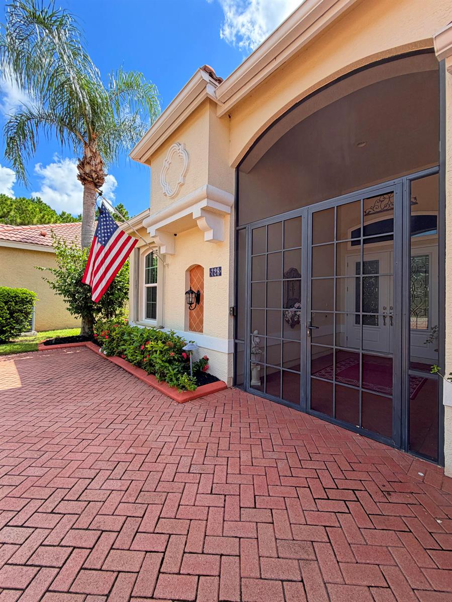A paved driveway leads to the front entrance of a house with a screened porch — 728 SW Lake Charles Circle, Port St. Lucie FL 34986, PORT ST. LUCIE, FL