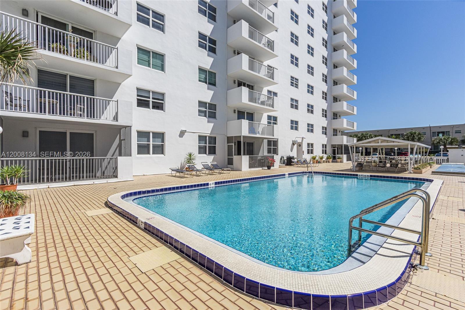 A swimming pool sits on a paved patio next to a multi-story white apartment building — 1601 S Ocean Dr # 305, Hollywood FL 33019, HOLLYWOOD, FL