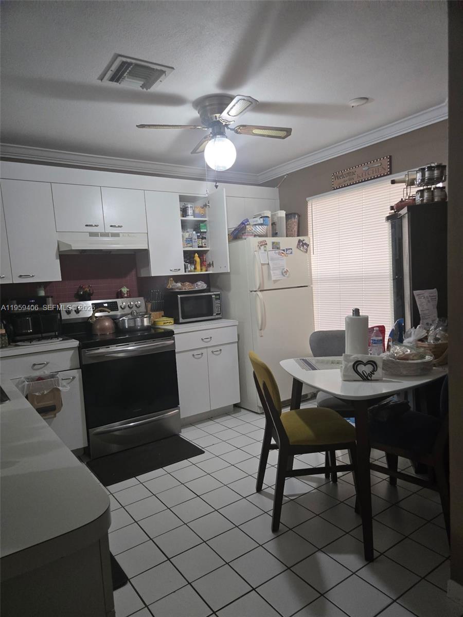 A kitchen features white cabinets, a black stove, a white refrigerator, and a small dining table — 4925 W Lakes Dr, Deerfield Beach FL 33442, DEERFIELD BEACH, FL