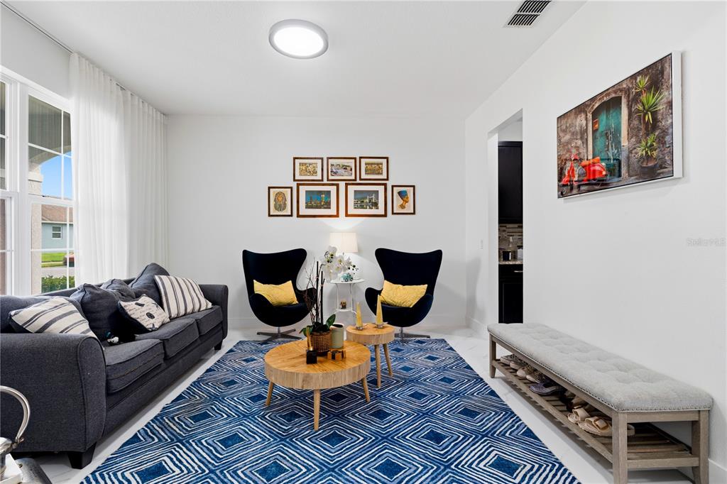 A living room features a blue patterned rug, a gray sofa, two black chairs, and a bench — 12225 STONE BARK TRAIL, ORLANDO, FL